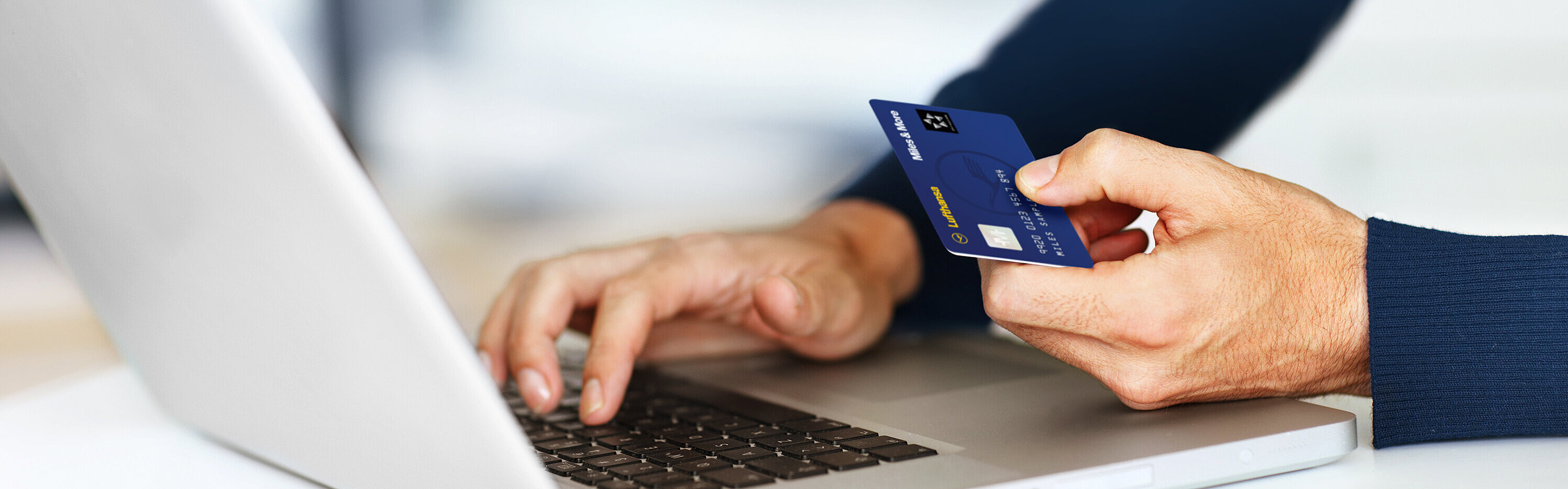 Person mit Laptop und Lufthansa Miles&More Kreditkarte