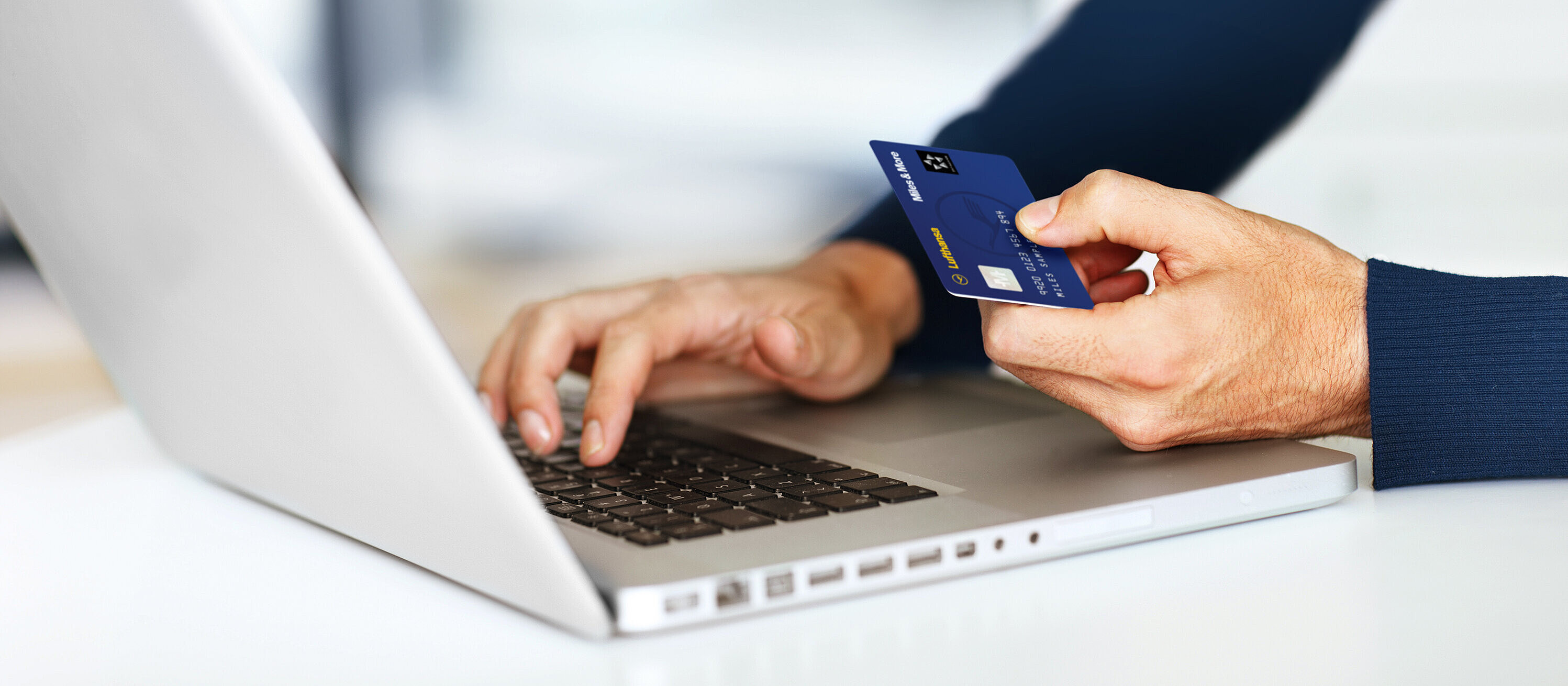 Person with laptop and Lufthansa Miles&More credit card