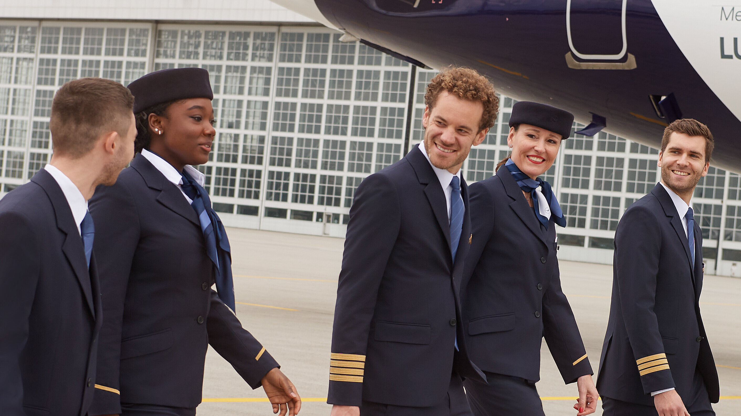 Fünf Lufthansa City Airlines Mitarbeitende, welche sich auf dem Vorfeld unterhalten, während sie ihr Gepäck mit sich führen