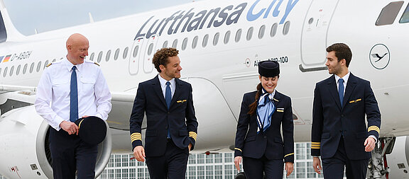 Vier Lufthansa City Airlines Mitarbeitende vor einem Airbus A319-100 auf dem Vorfeld