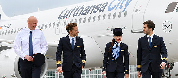 Vier Lufthansa City Airlines Mitarbeitende vor einem Airbus A319-100 auf dem Vorfeld