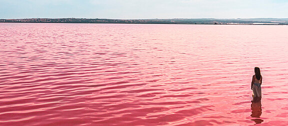 Eine Person steht in rot eingefärbten Meer bei Alicante in Spanien unter leicht bewölktem Himmel