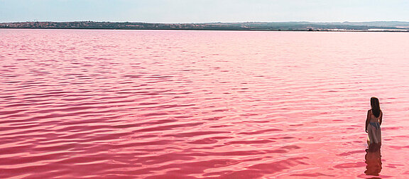 A person stands in red coloured sea near Alicante in Spain under slightly cloudy sky