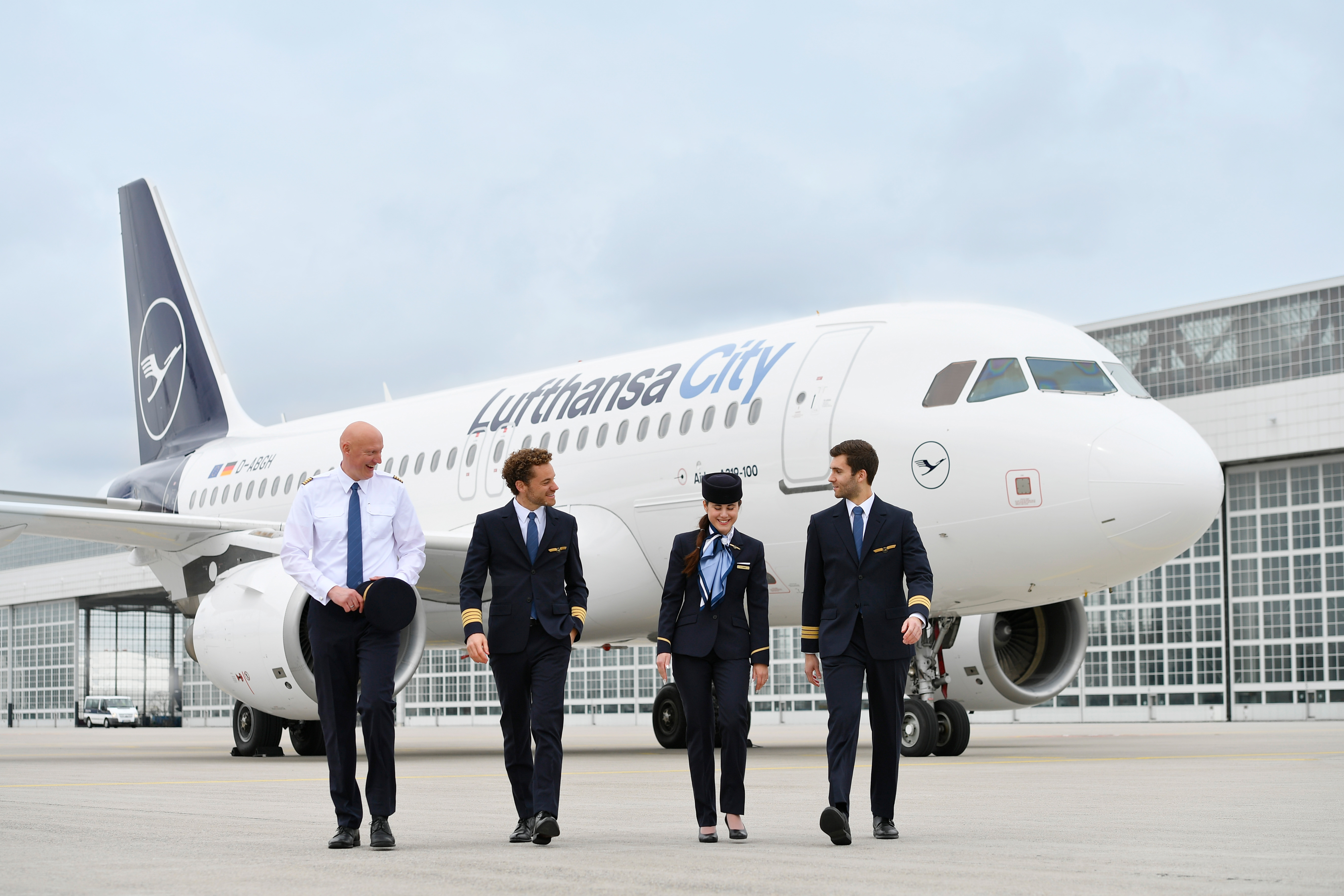 Vier Lufthansa City Airlines Mitarbeitende vor einem Airbus A319-100 auf dem Vorfeld